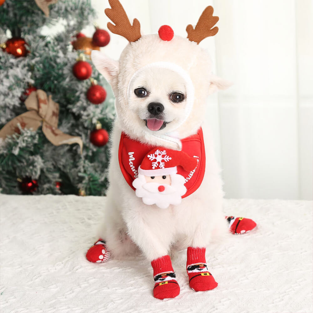 Small dog wearing full reindeer pet costume set including socks, hat, bib, and shoes while sitting on festive blanket