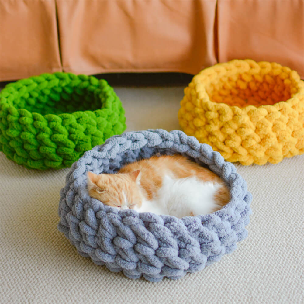 A gray handwoven round cat nest with a small kitten curled inside.