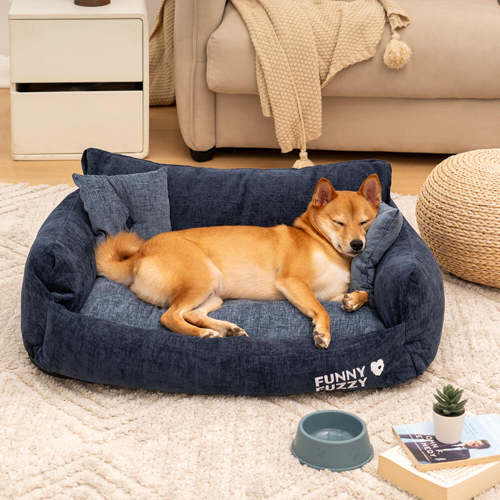 A comfortable, vintage-style chenille pet sofa bed in a warm beige color, featuring two matching pillows, viewed from the front-side angle in a cozy living room setting.