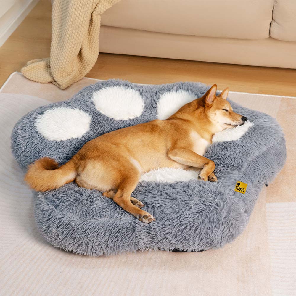 Small brown dog sleeping soundly on a fluffy paw-shaped washable dog bed